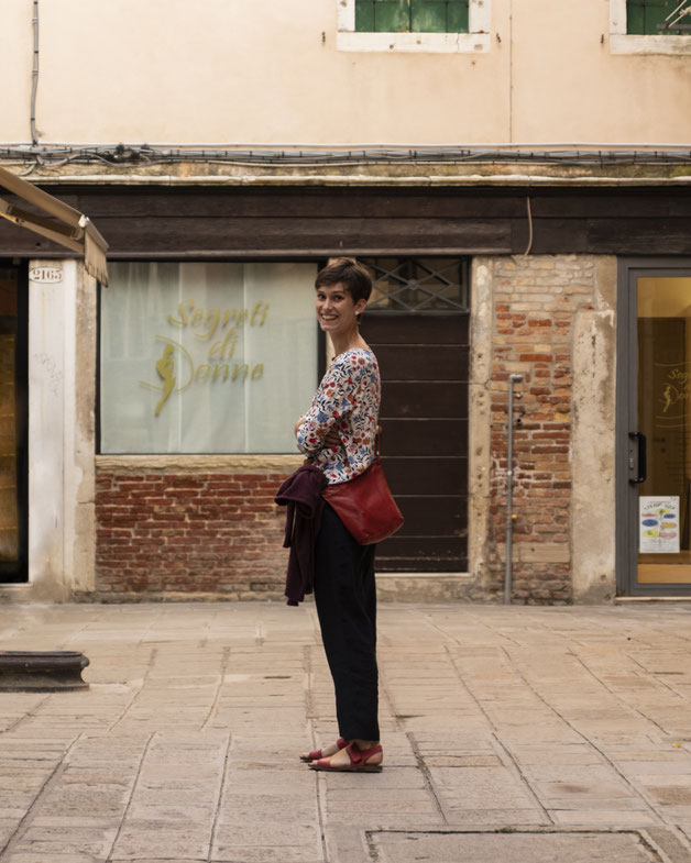 Foto von Sofie Mück, einer jungen Frau in einer italienischen Altstadt. Sie ist sommerlich gekleidet und lächelt in die Kamera.